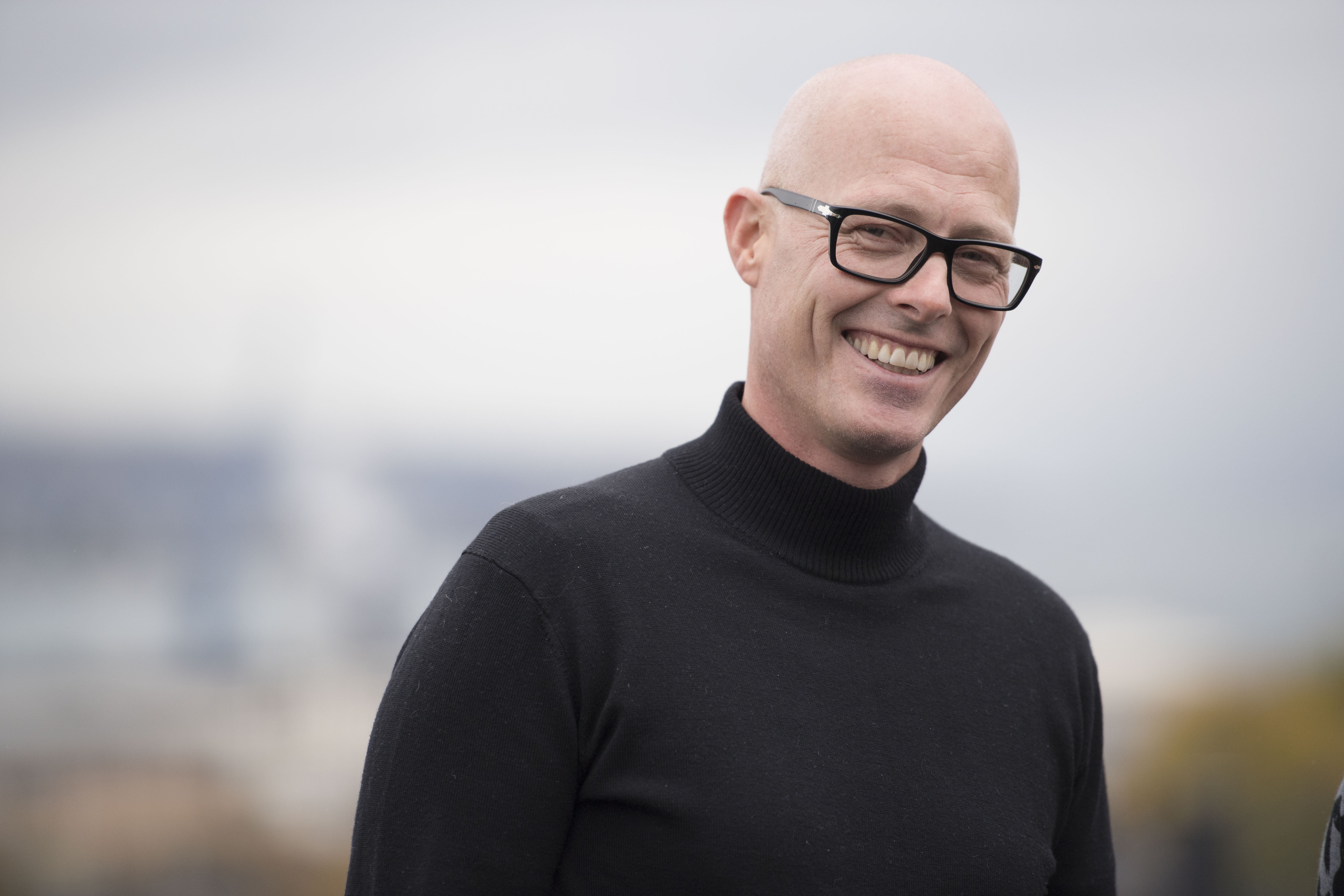 Person med svart høyhalset genser står ute med uskarp bybakgrunn.